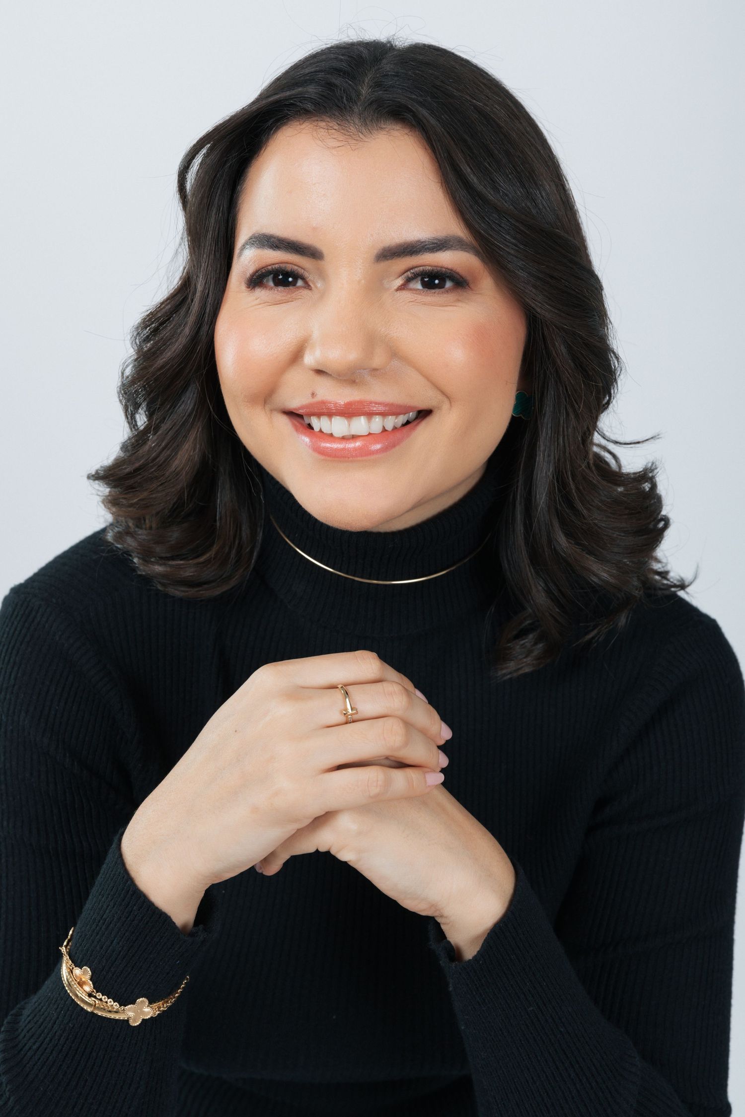 Studio headshot in black turtleneck with jewelry and natural makeup.
