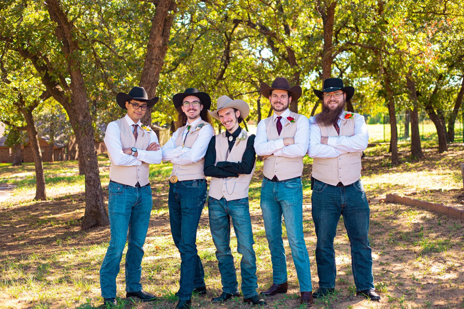 Groomsmen in matching western outfits with cowboy hats posing in outdoor setting.
