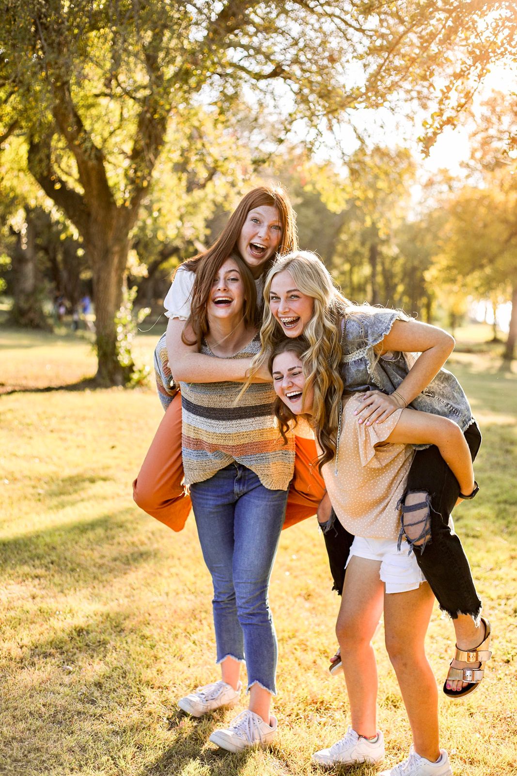 Friends laughing and playing piggyback in a sun-drenched park during autumn.