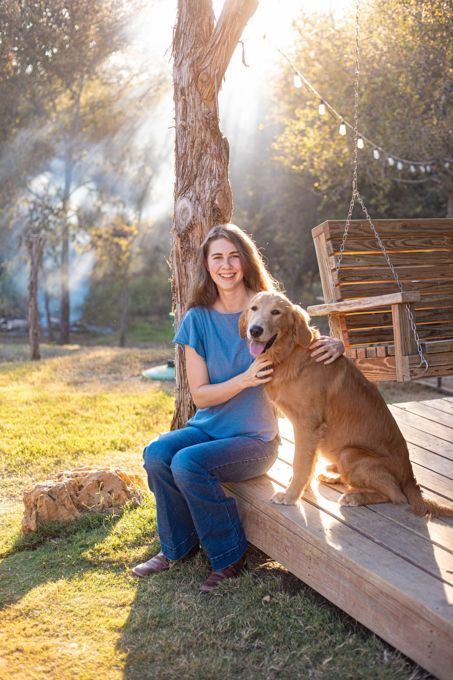 Person in blue top sitting with friendly golden retriever on outdoor wooden deck.