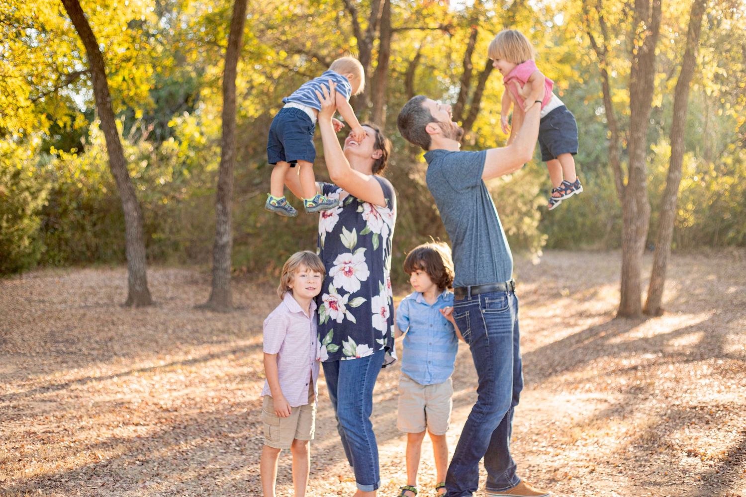 Family members playing and being lifted up against a backdrop of golden autumn trees.