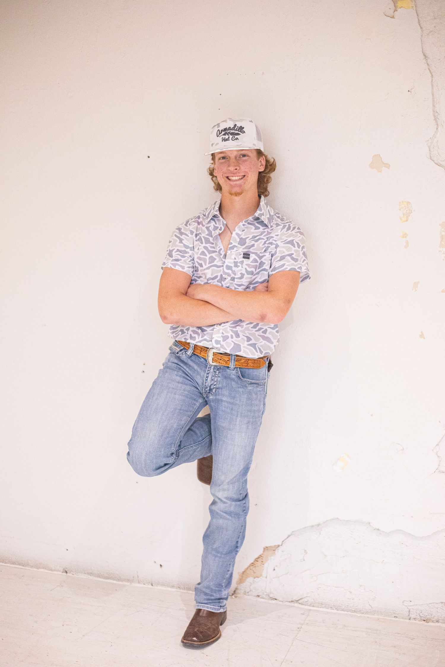 A casual portrait against a white wall showing someone in jeans and a patterned shirt.