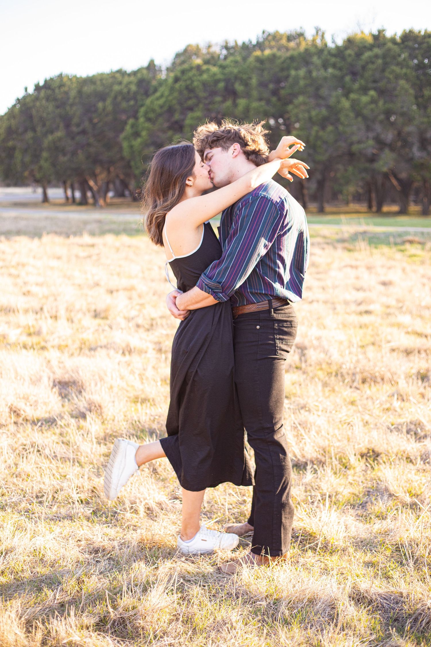 A romantic embrace in a golden field with trees in the background.