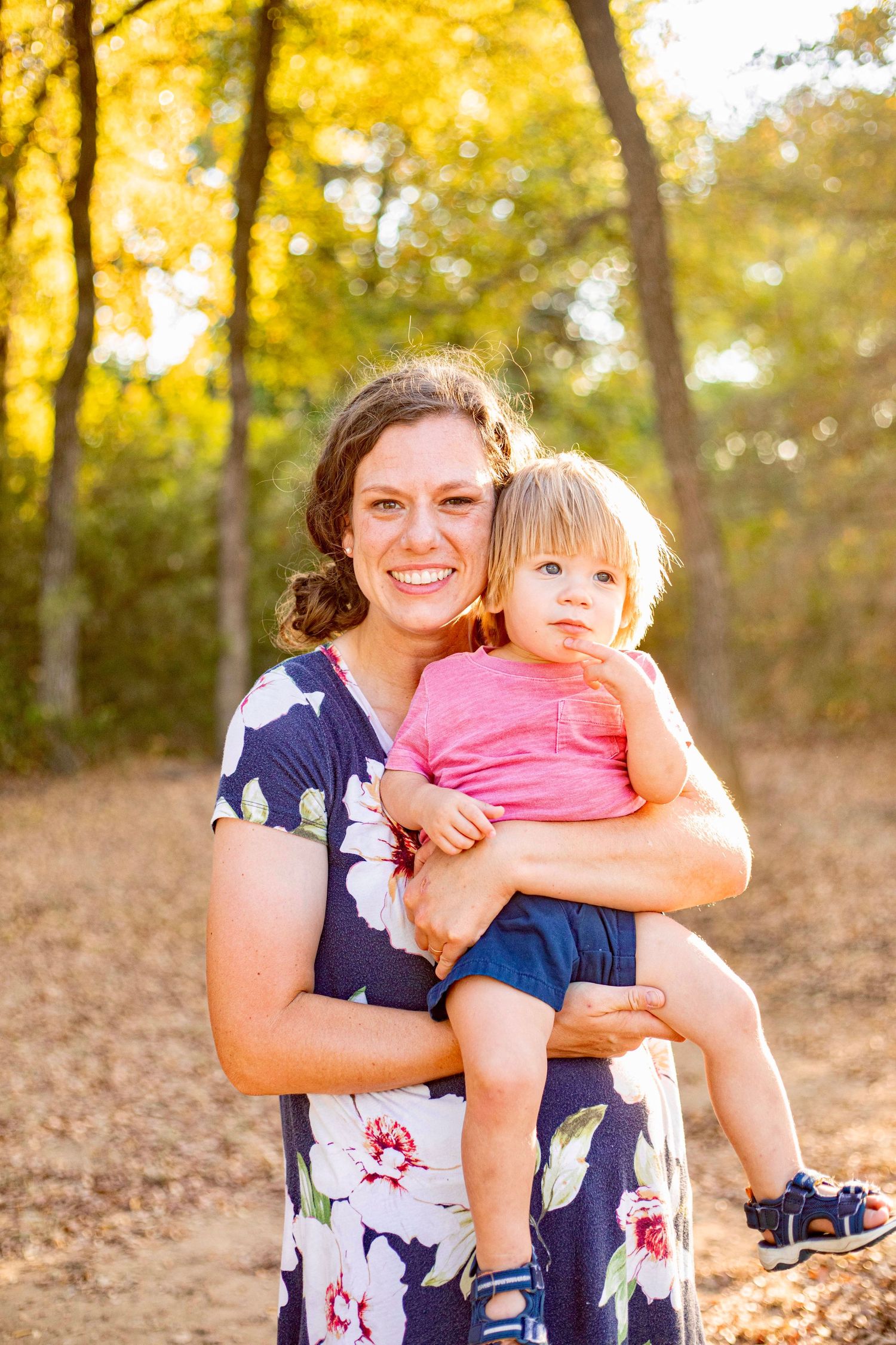 A tender family moment captured in warm autumn sunlight with fallen leaves on the ground.