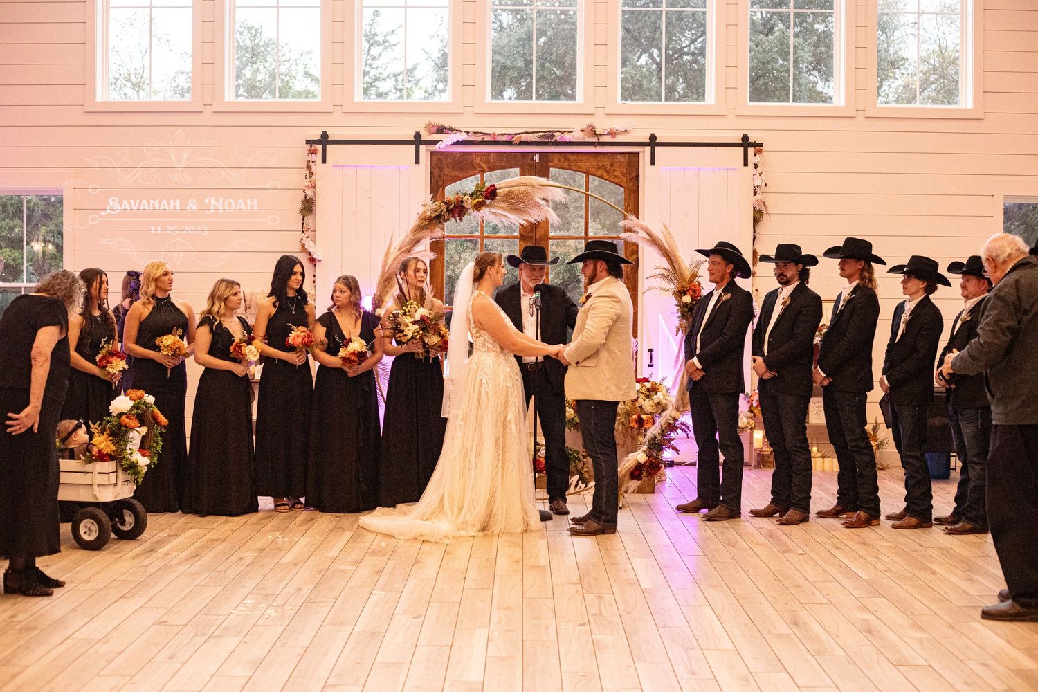 Wedding ceremony in a rustic indoor venue with wooden arch and matching wedding party attire.