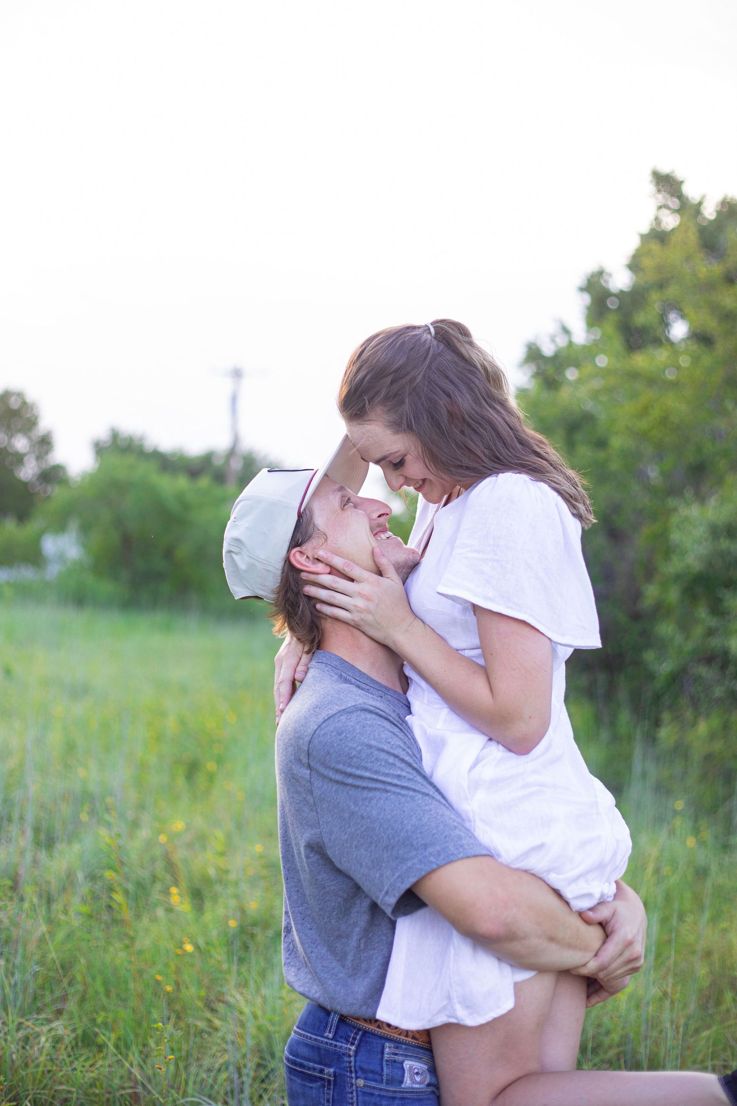 A romantic couple shares tender embraces in a sunny field during their photoshoot.