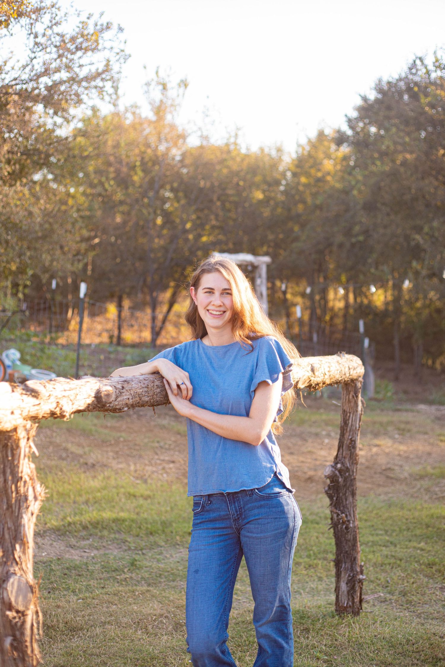 Person in blue shirt posing with fallen log in autumn outdoor setting.