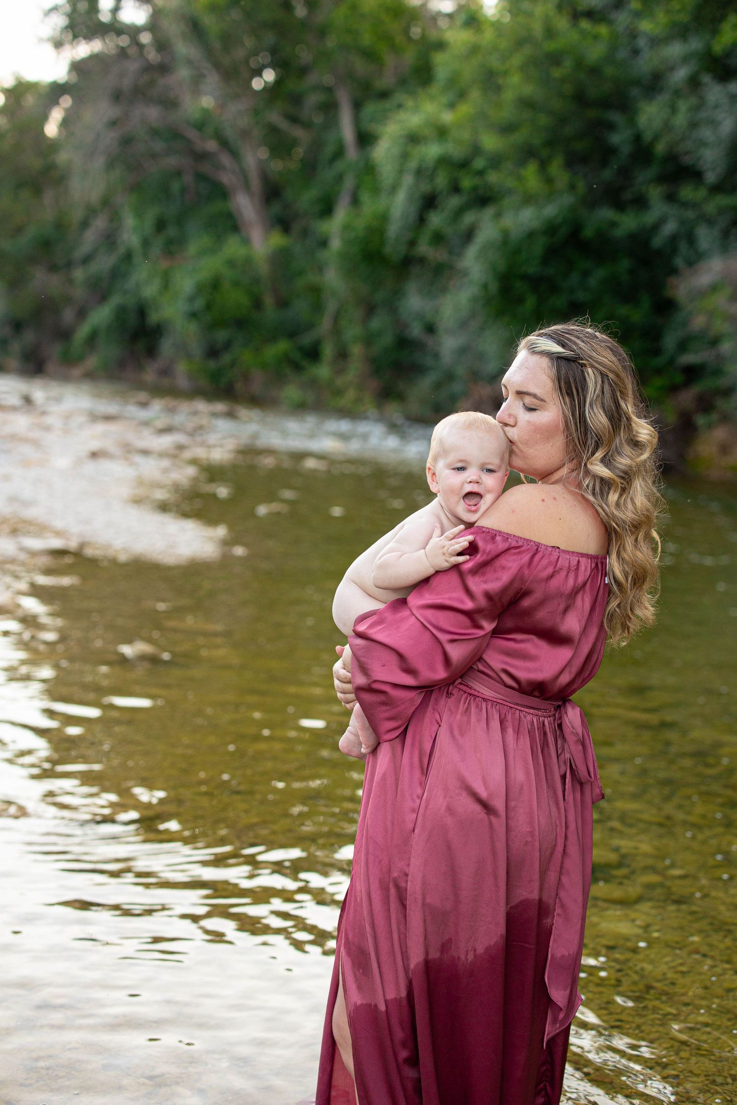 A touching moment captured against a backdrop of trees and water with pink and denim attire.