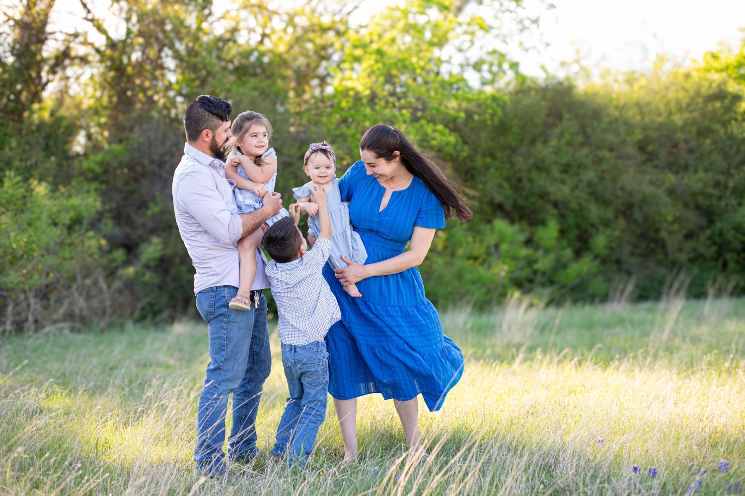 Happy family of four playing in a sunny green meadow, parents and children enjoying outdoor time together.