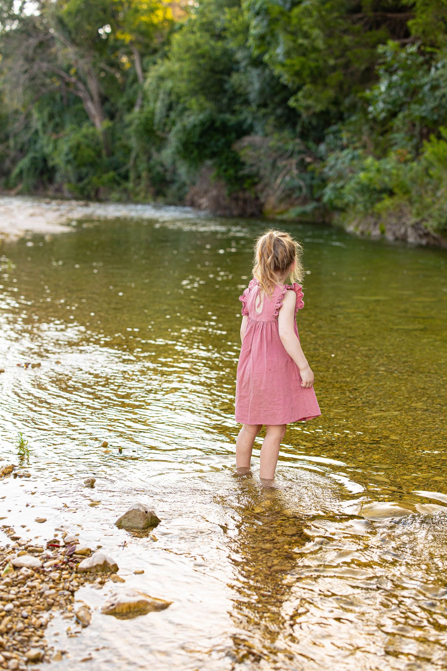 Children playing in shallow river water wearing matching pink dresses.