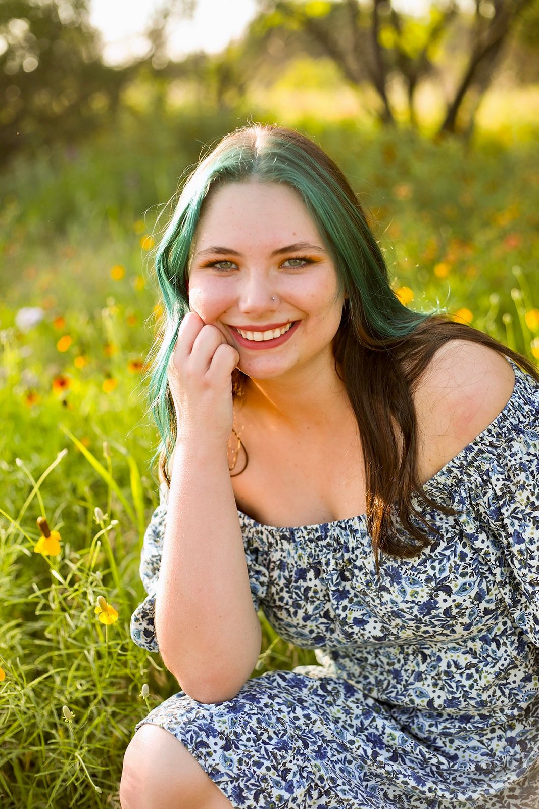 A person in a floral dress poses playfully in a sunny field with yellow wildflowers.