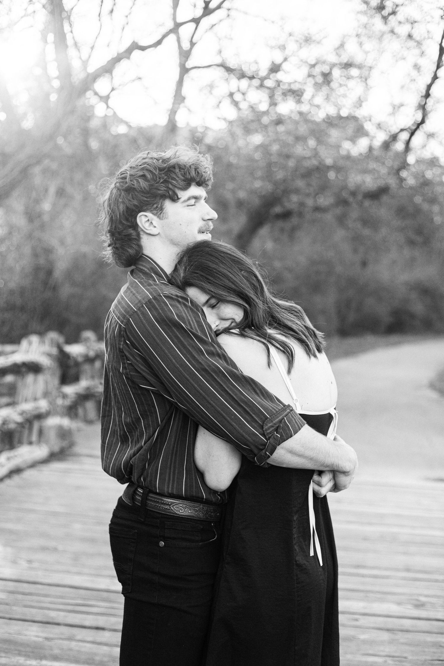 A couple embraces in a tender black and white moment on a wooden walkway.