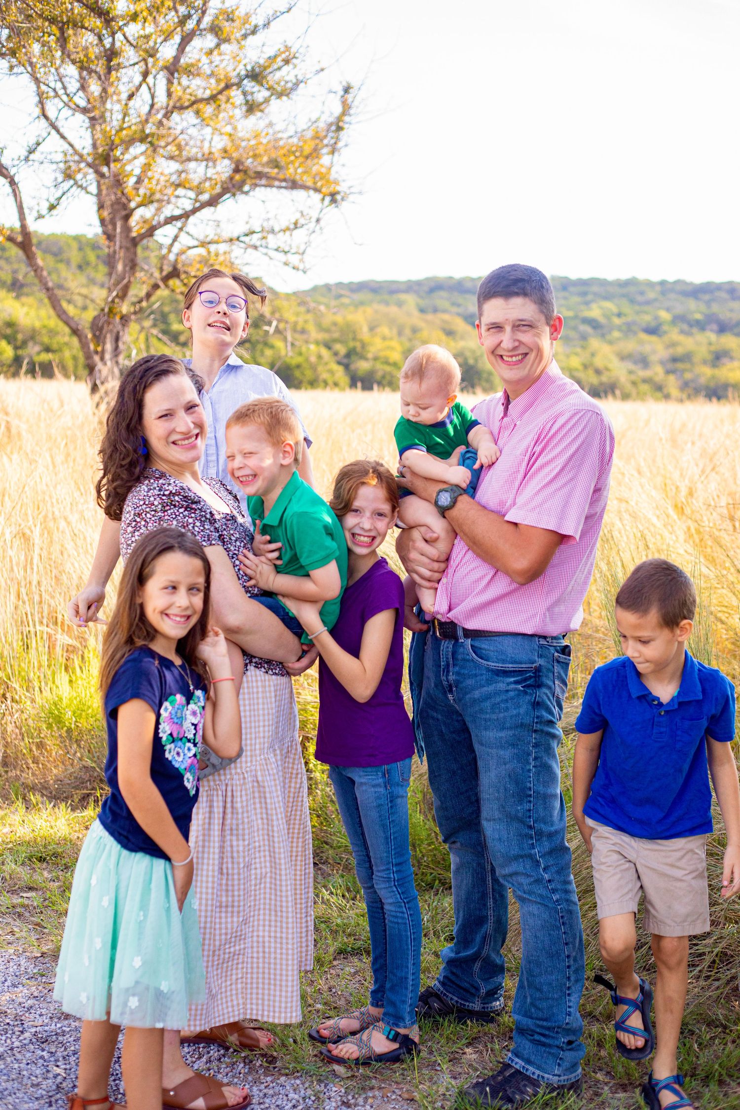 Family group laughs together while posing in tall golden grass at sunset.