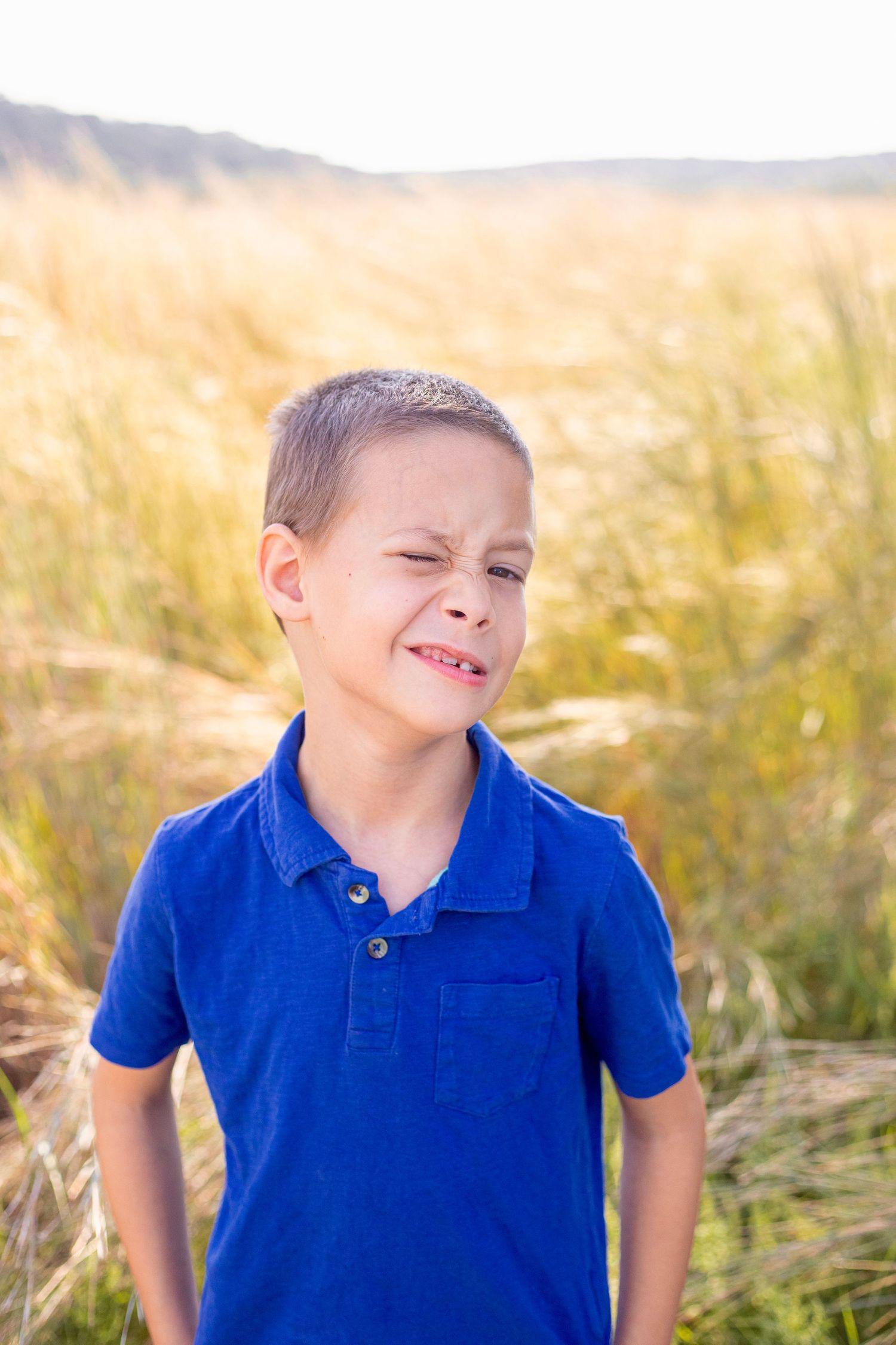A child in a blue polo shirt laughs joyfully in a wheat field.