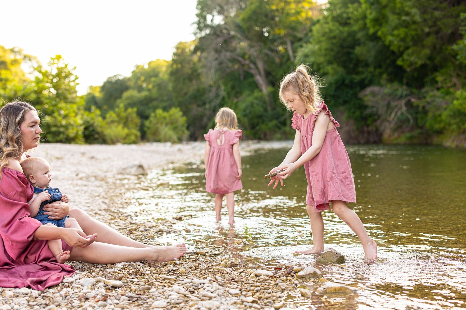 A peaceful scene by the river with people in matching pink dresses enjoying a summer afternoon on the rocky shore.