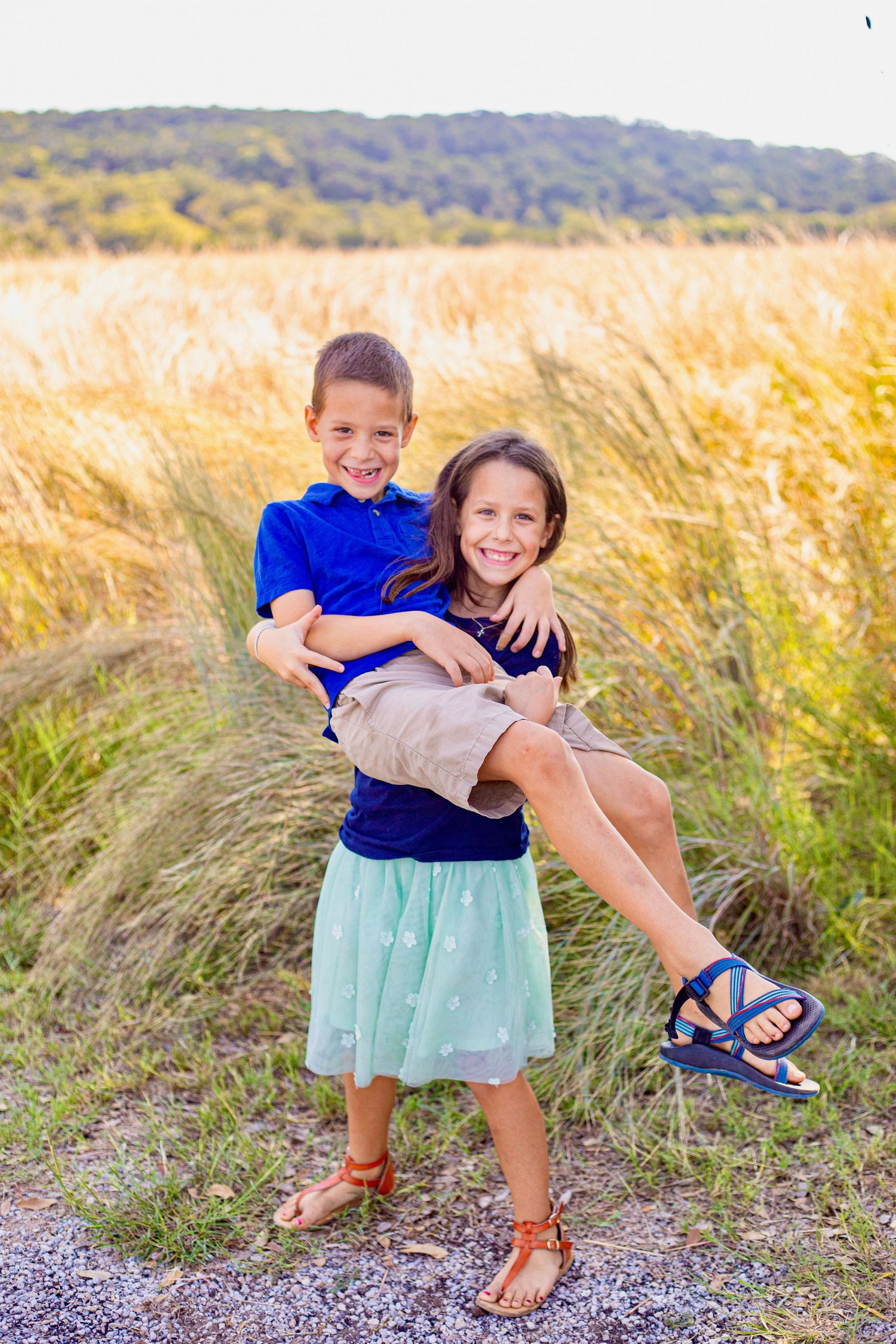 Playful interactions on a gravel path with golden grass and rolling hills in the background.