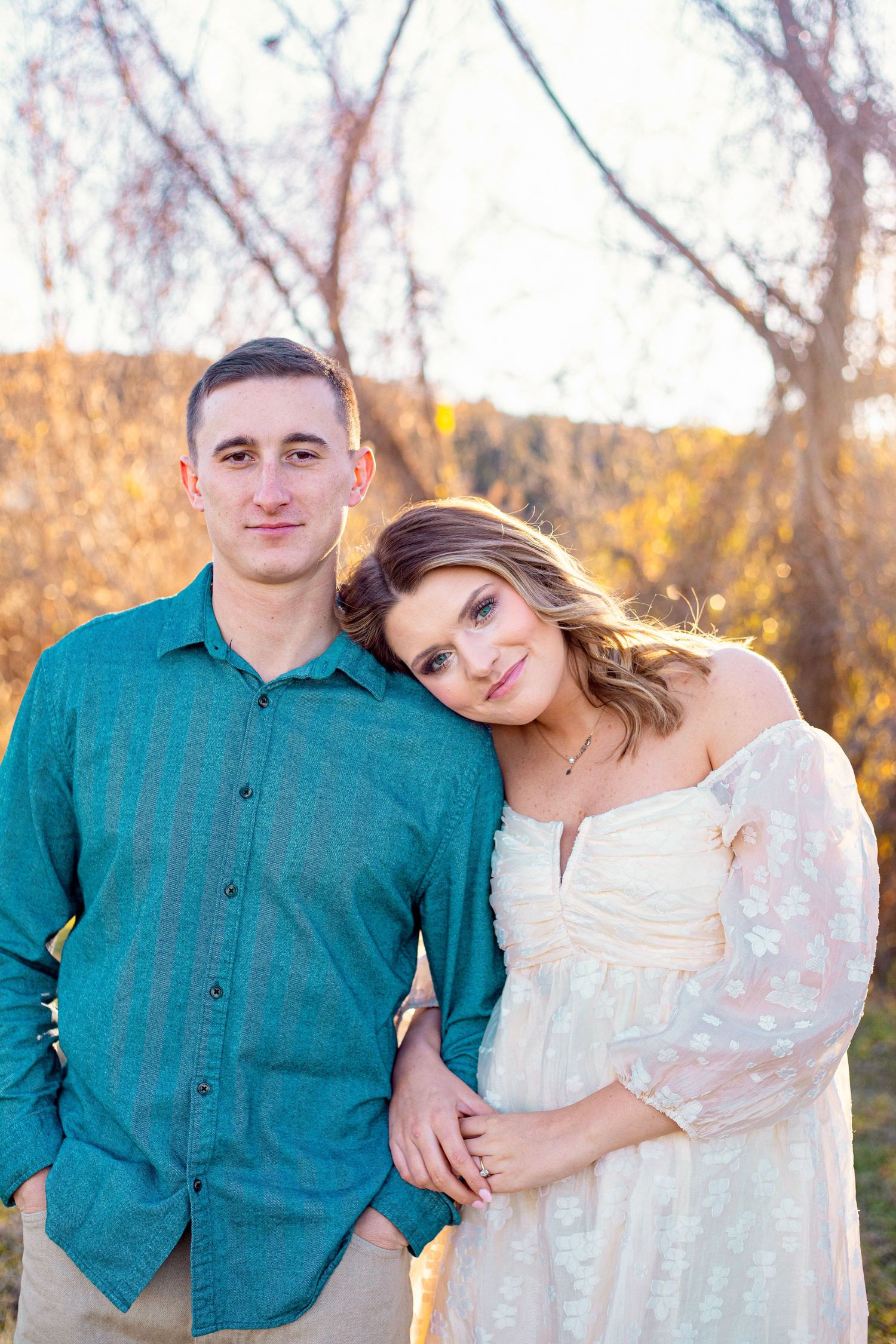A couple poses together during golden hour in autumn, wearing coordinated teal and white outfits.
