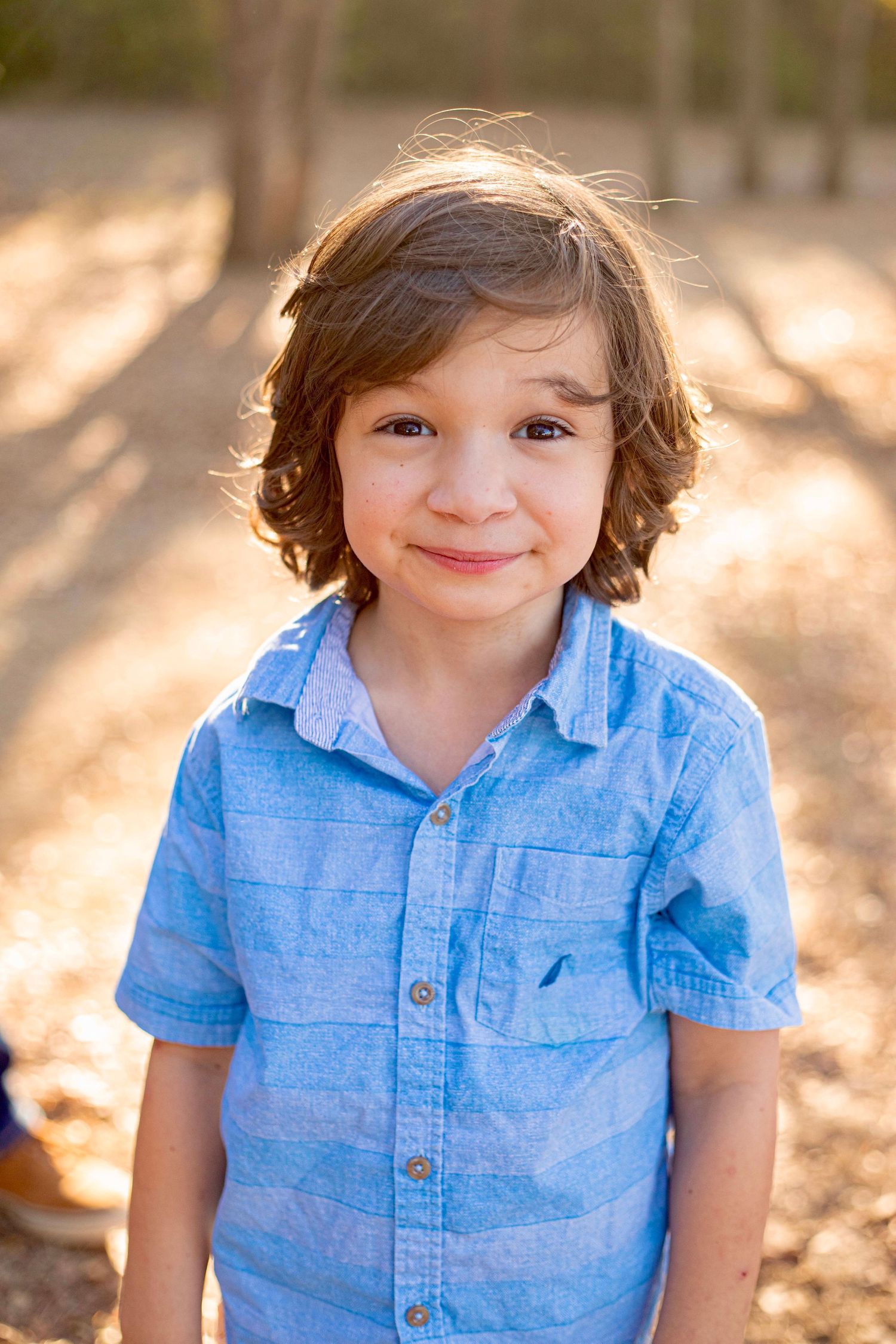 A child in a blue striped shirt smiles warmly during an outdoor autumn photoshoot.