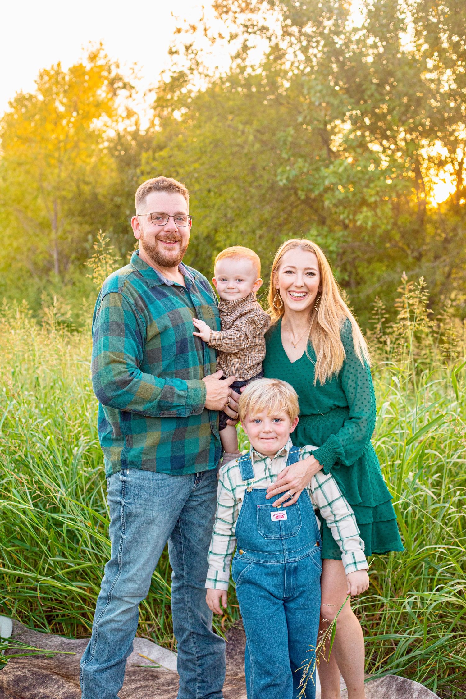 Family in coordinating outfits poses together in tall grass during sunset photo session.