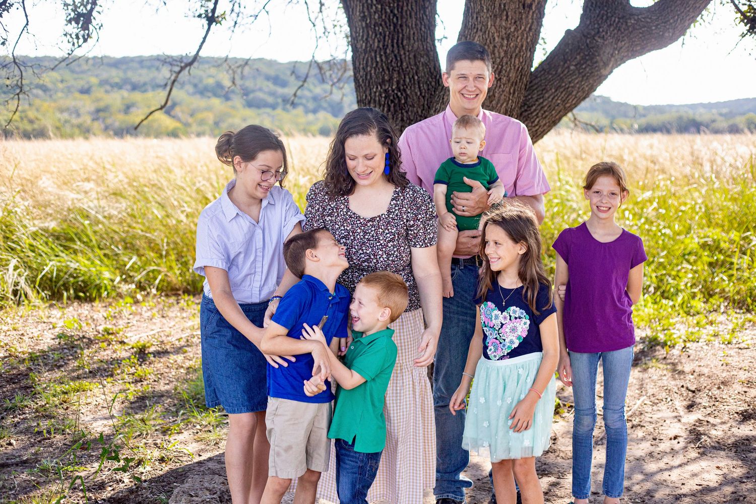 Casual outdoor family gathering beneath a large oak tree in natural lighting.