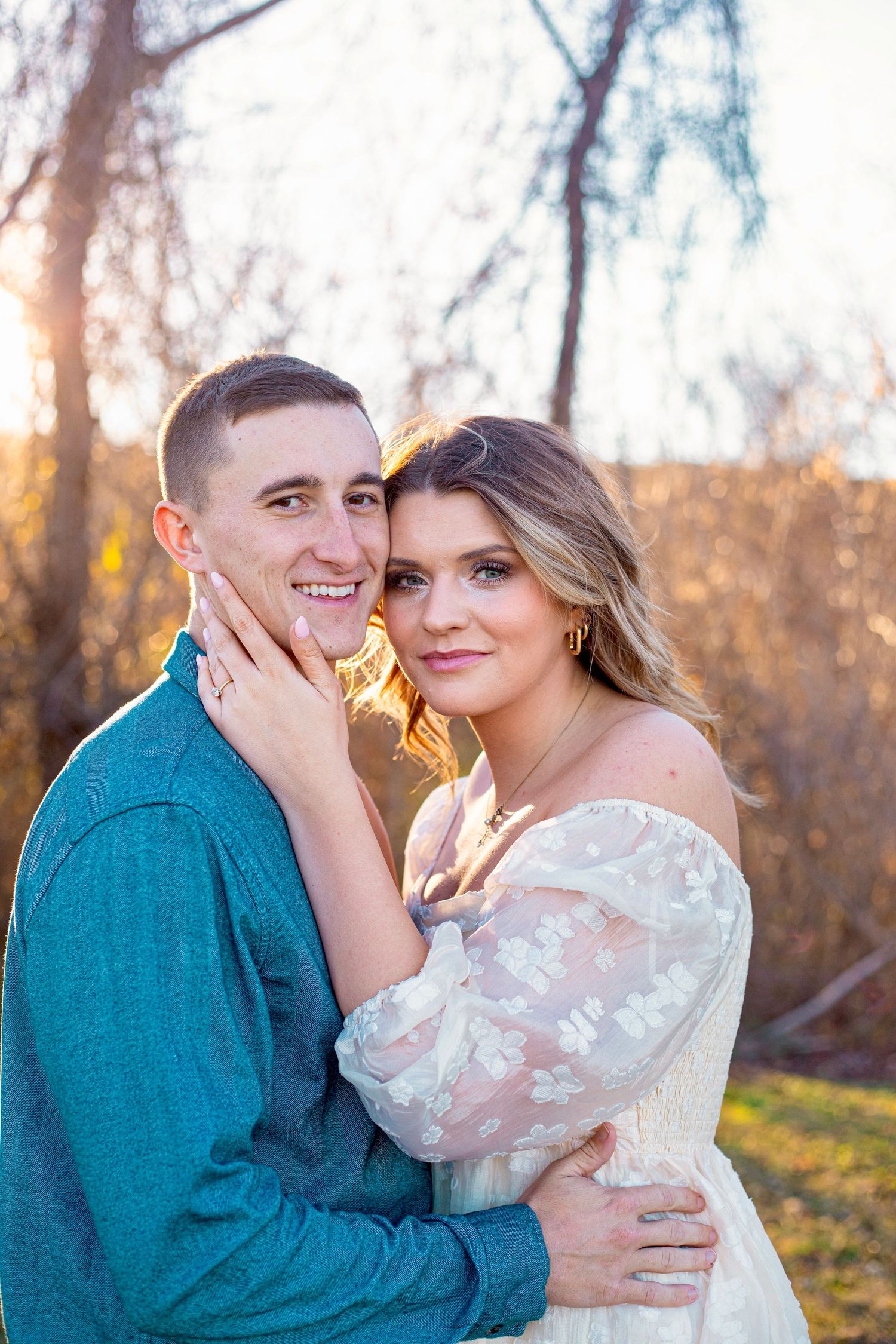 A close-up portrait of a couple smiling during golden hour with autumn colors in background.