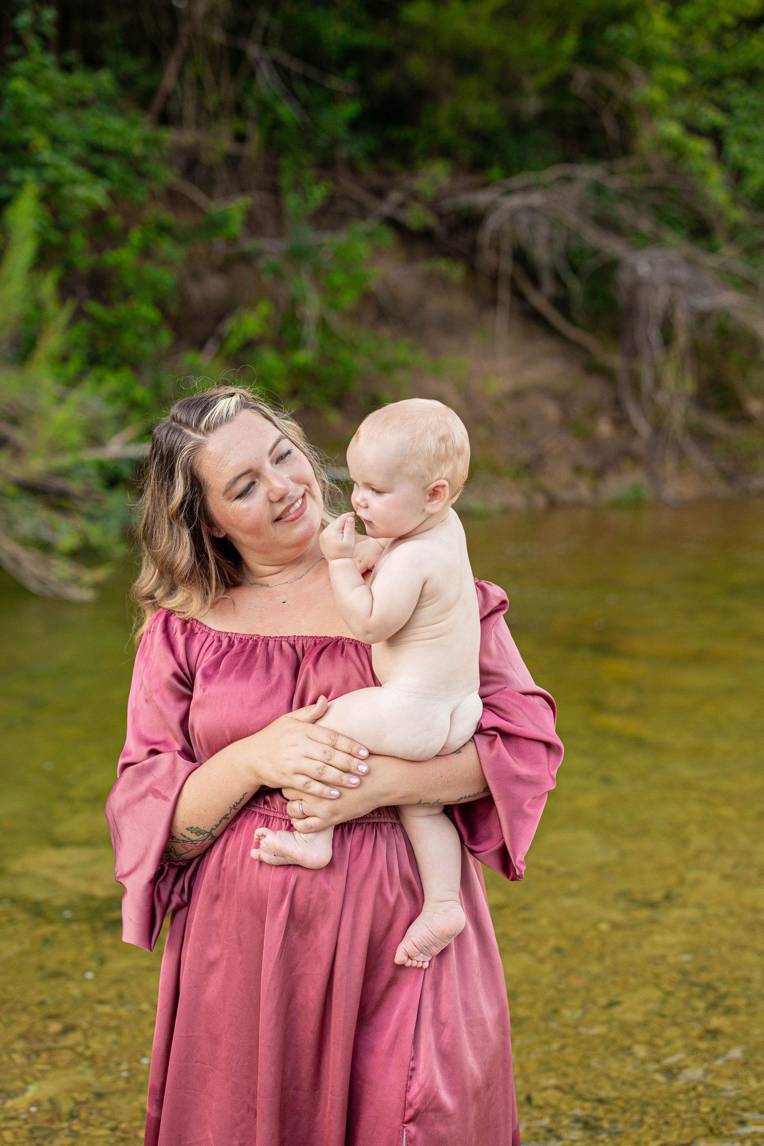 Joyful outdoor photoshoot in a burgundy dress by a scenic riverbank.