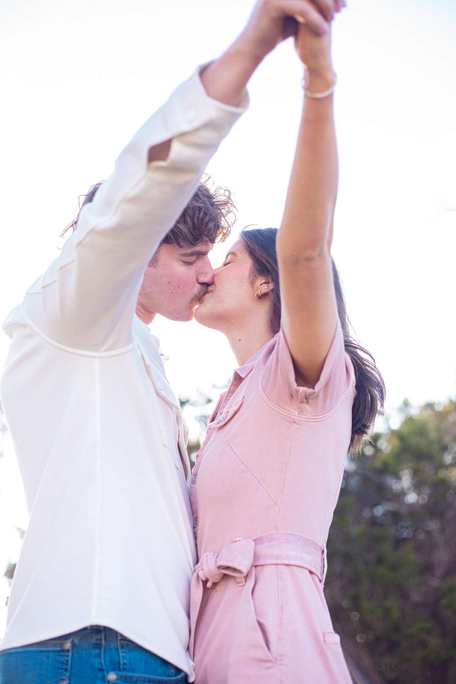 Couple dancing together outdoors with arms raised against bright sky.