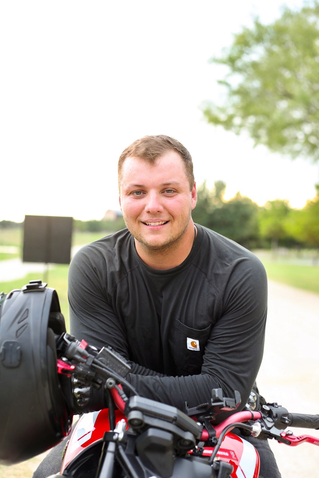 Person in black shirt posing with a motorcycle outdoors.