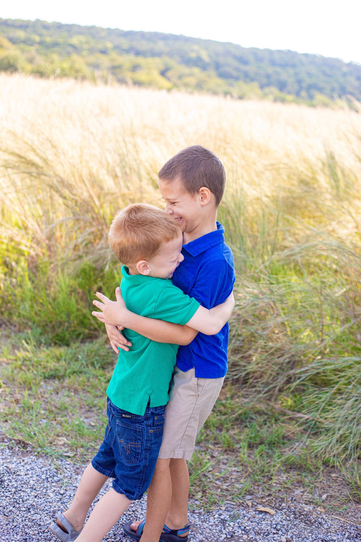 Two children hugging and playing together in a scenic outdoor setting with tall grass.