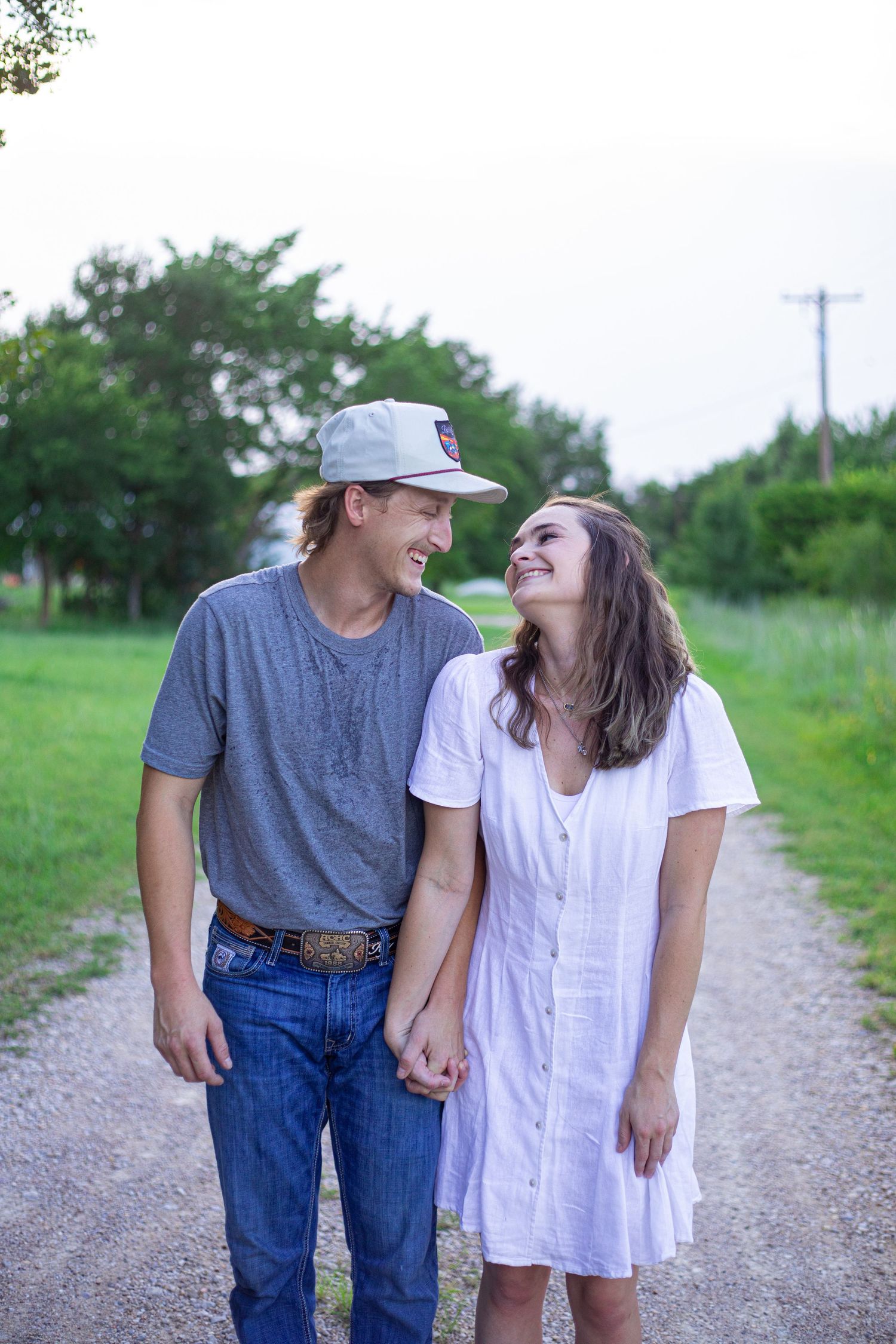 A couple walks and laughs together on a gravel path surrounded by greenery.