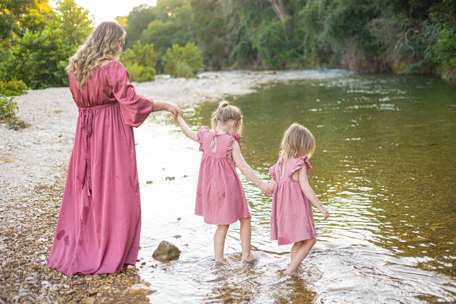 People in coordinating pink outfits explore the shallow waters of a scenic river.