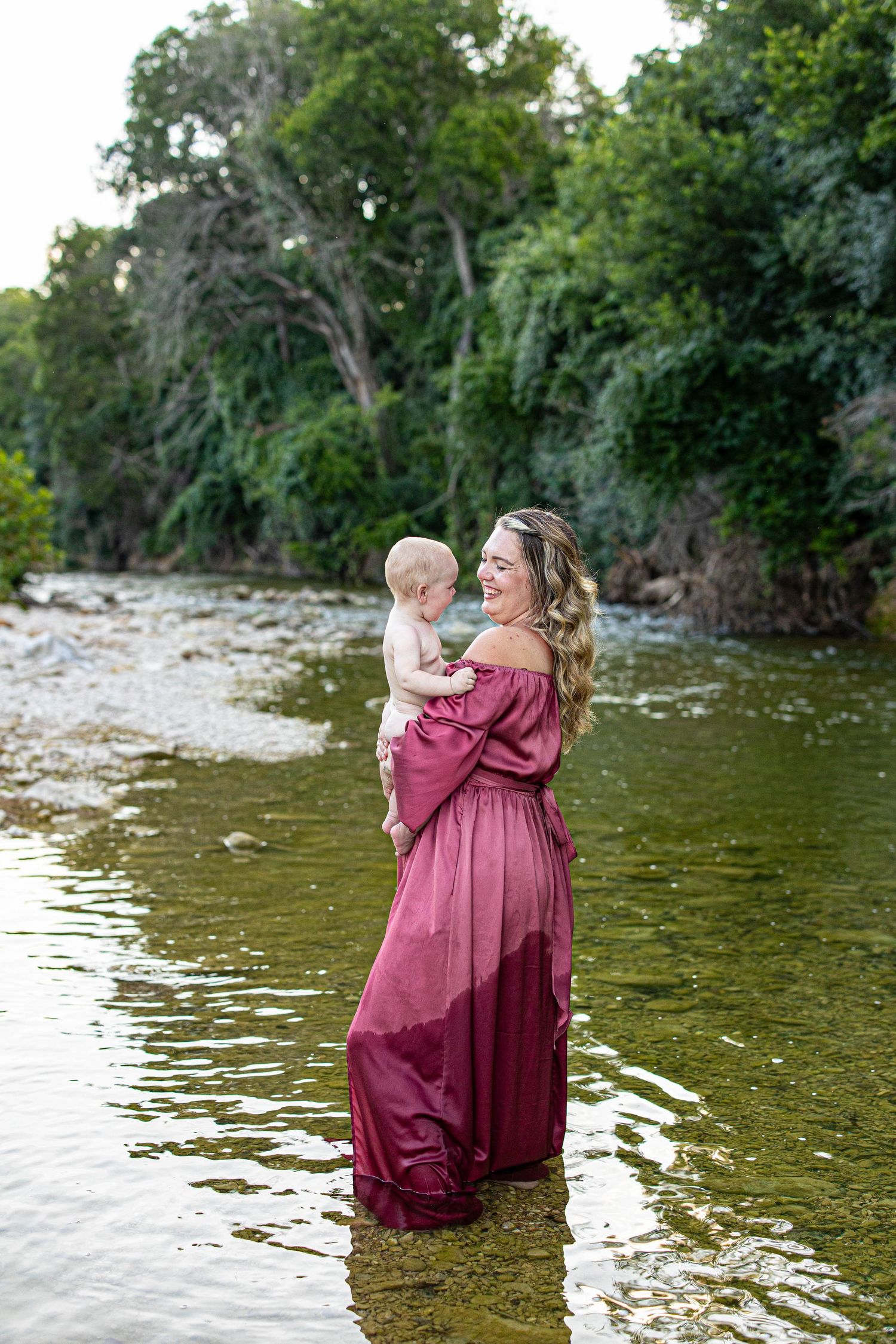 A tender moment captured in a flowing burgundy dress by the water's edge.