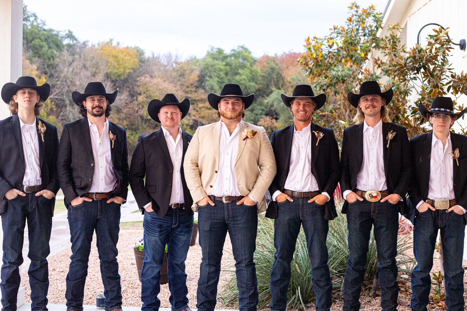 Groomsmen in western attire with cowboy hats and jeans posing outdoors.