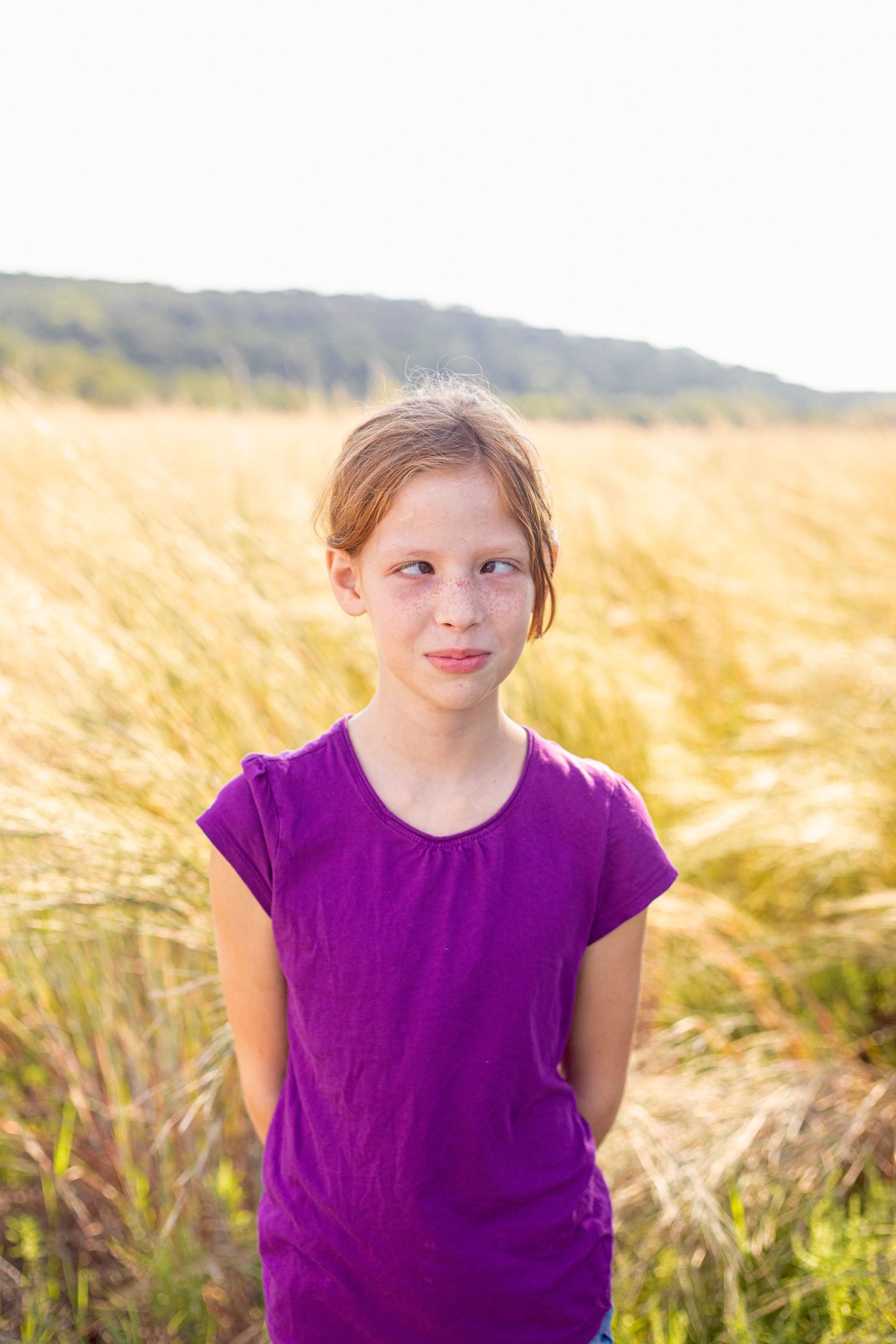 A person in a purple shirt stands among golden wheat at sunset.