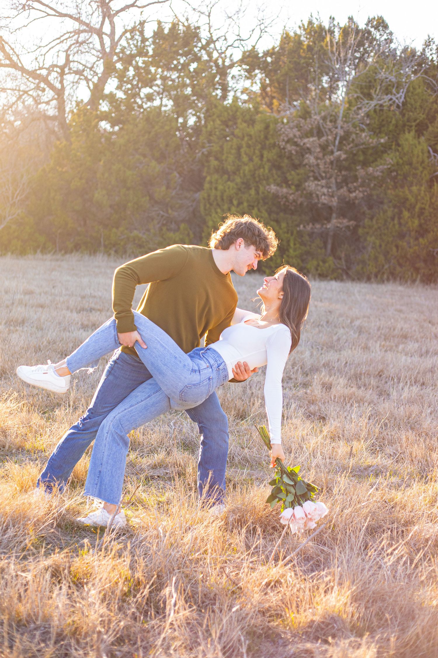 A romantic dip pose in a sunlit field with golden grass and pine trees.