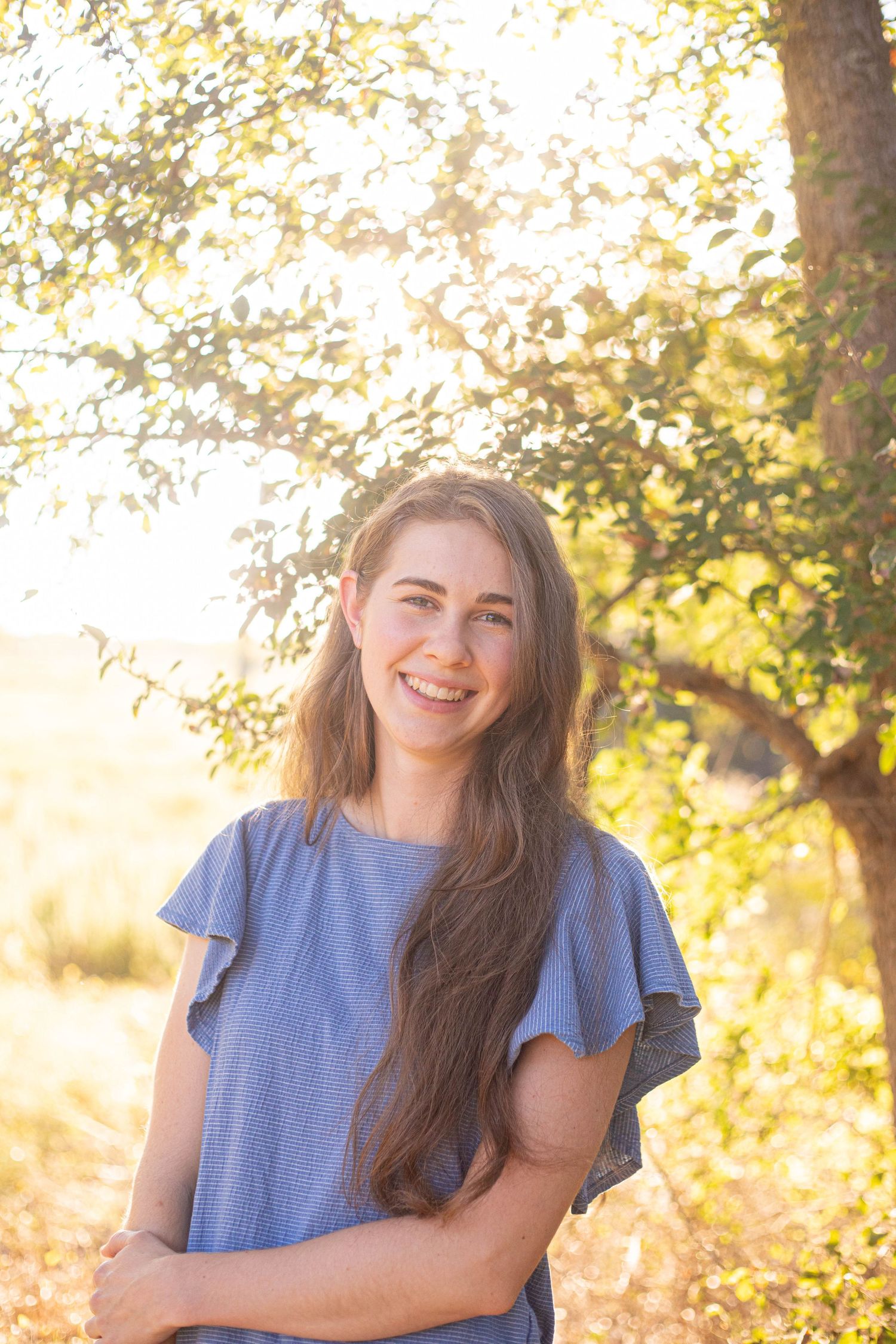 Candid outdoor portrait in denim outfit against golden sunlit trees and foliage.