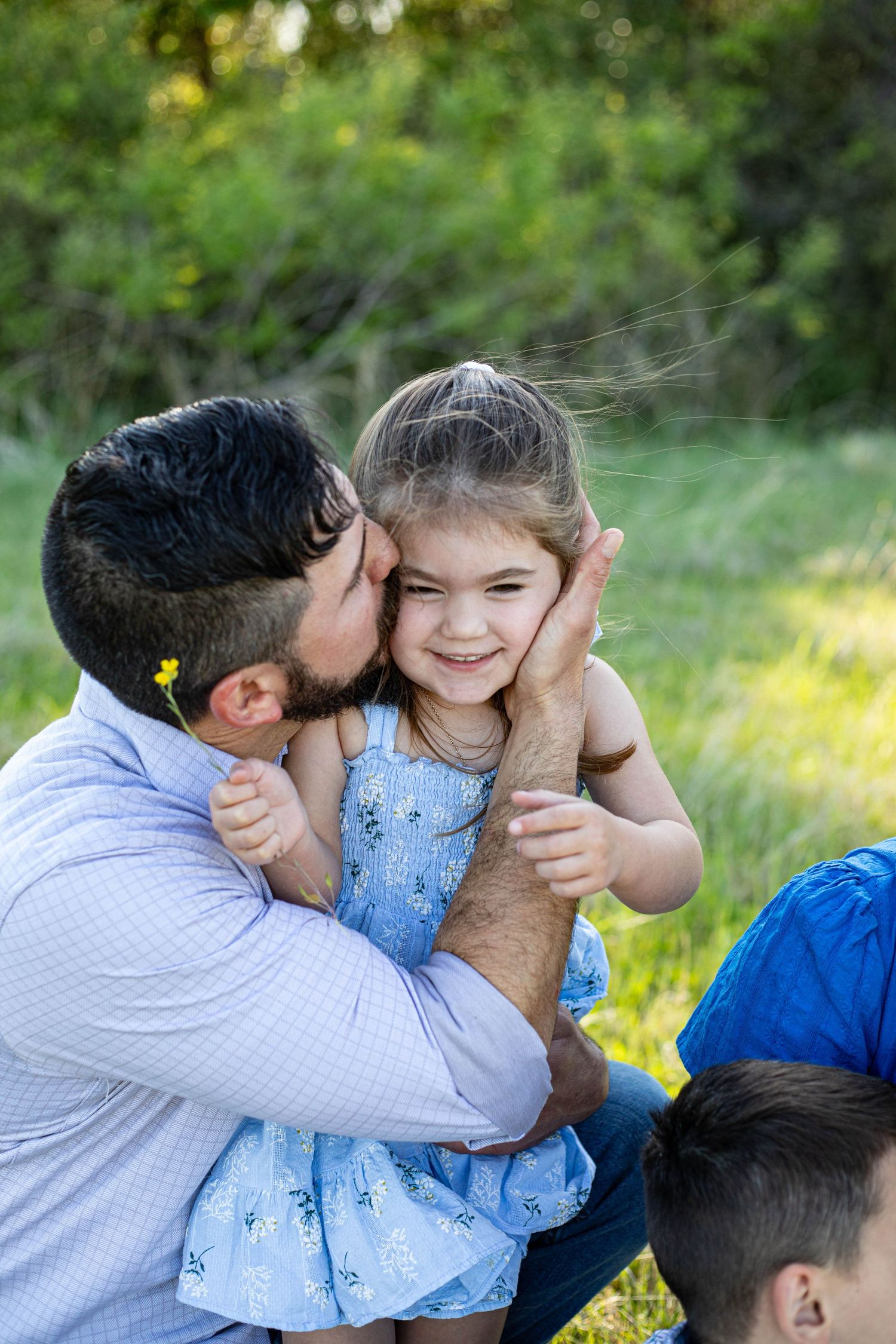 Loving father kissing his smiling young daughter on the cheek during a family photo session outdoors.
