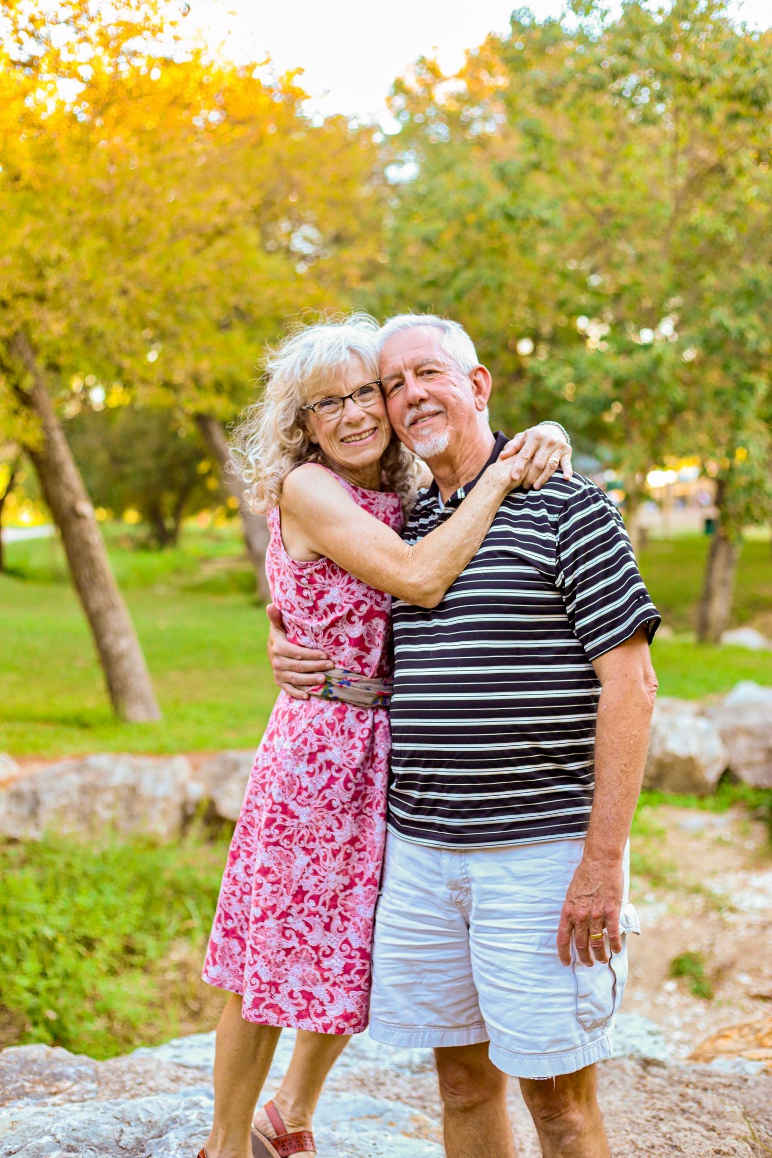 Senior couple embraces outdoors during golden hour among autumn trees.