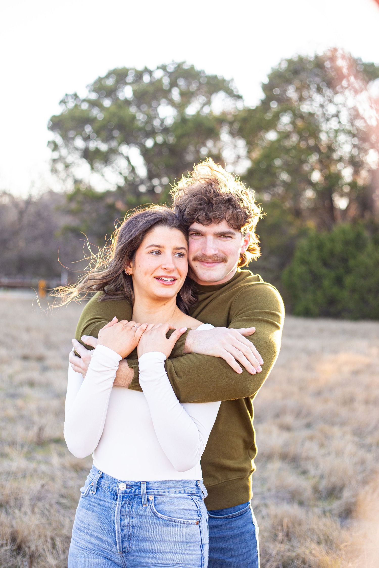 Playful couple laughing and hugging in an outdoor setting with natural sunlight.