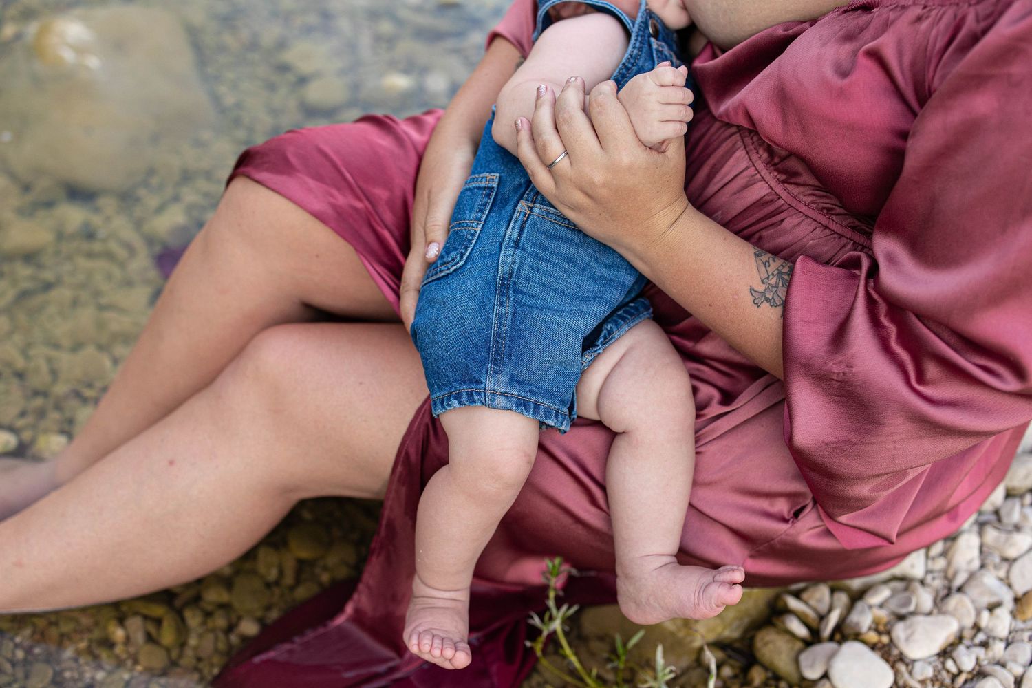 Close-up detail of denim overalls and a flowing pink dress against a rocky riverbank.