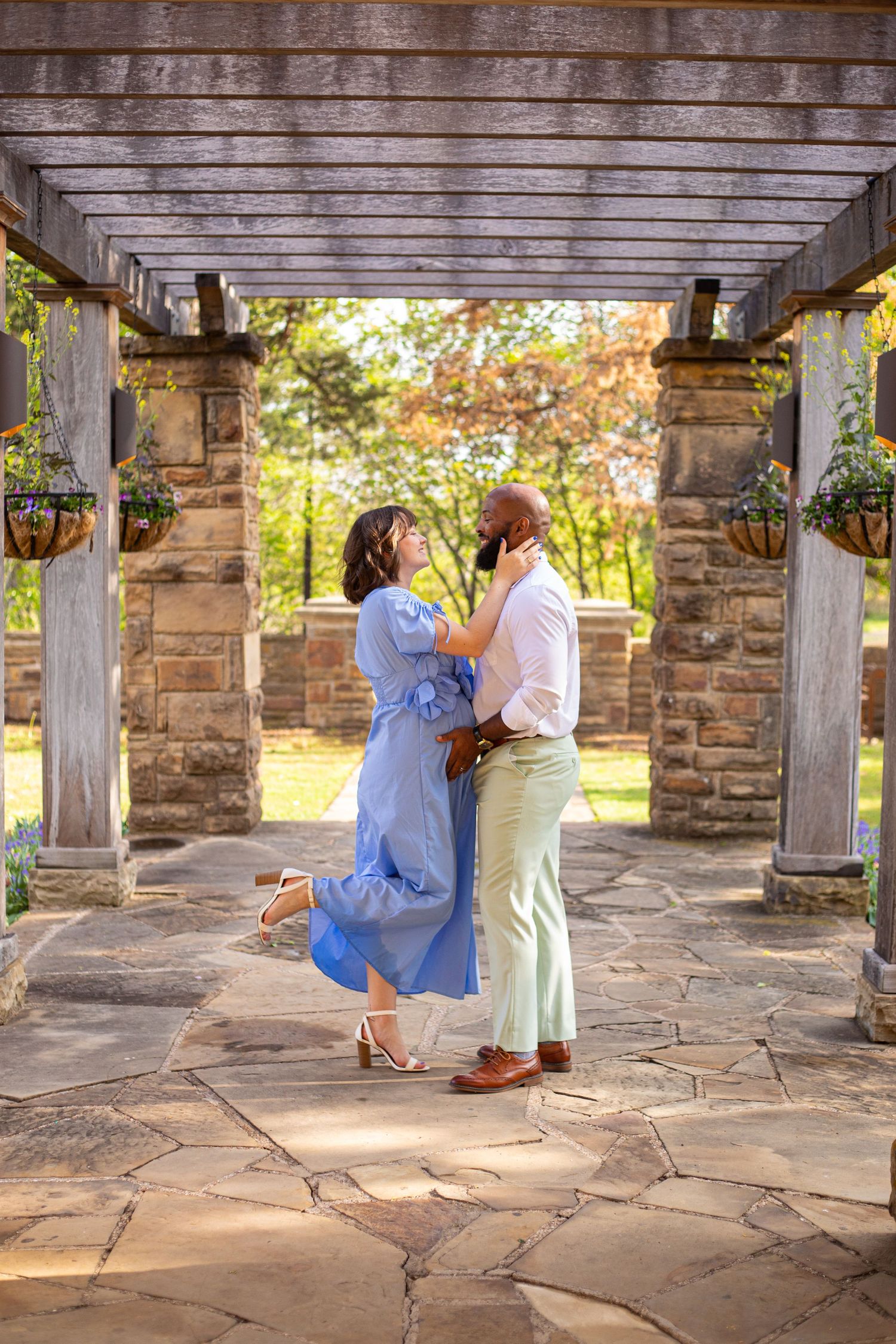 A romantic moment under a pergola with stone pillars and hanging plants.