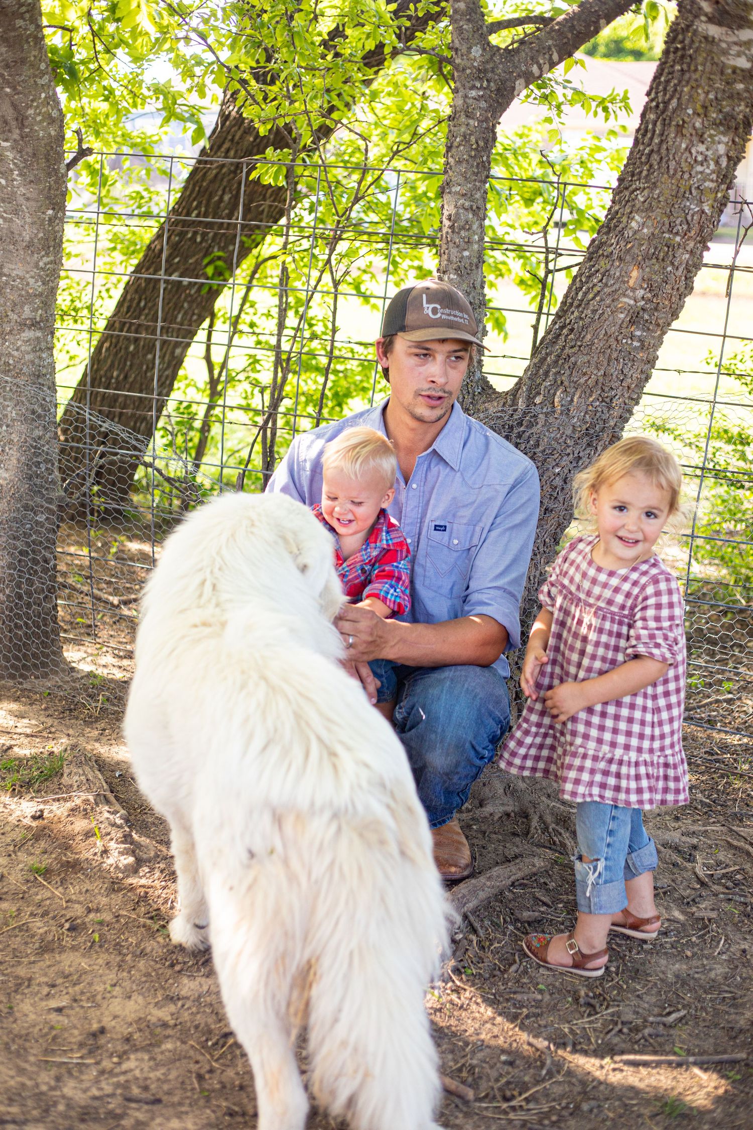 Family spending time with a large white farm dog in a wooded area.