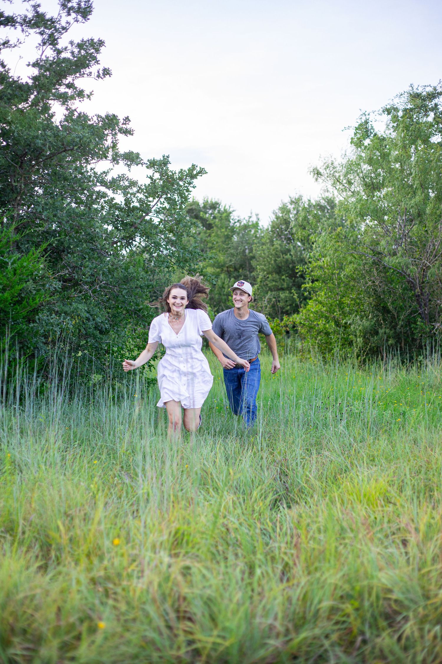Couple running through tall grass field during sunset.