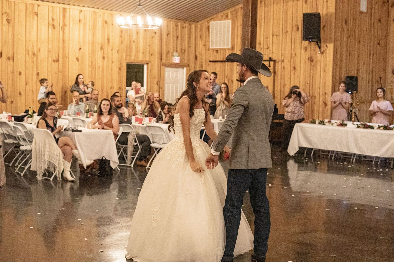 Wedding reception celebration inside rustic wooden barn venue with string lights.