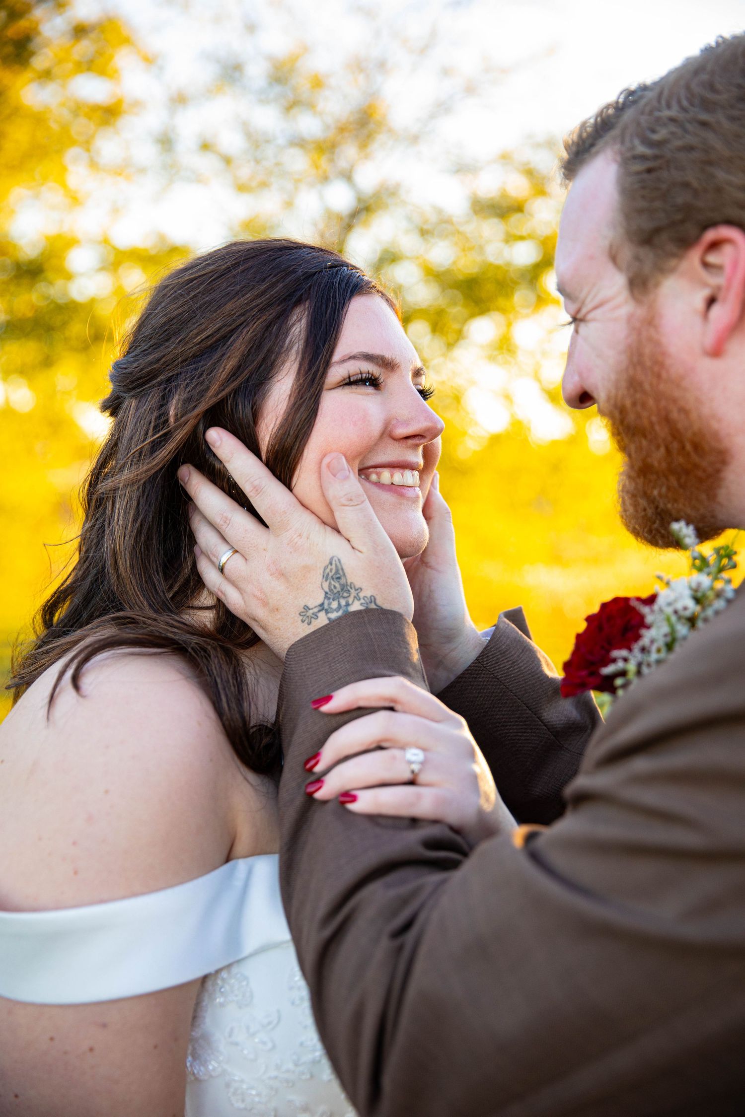 A groom tenderly cups his smiling bride's face during their fall wedding ceremony outdoors.