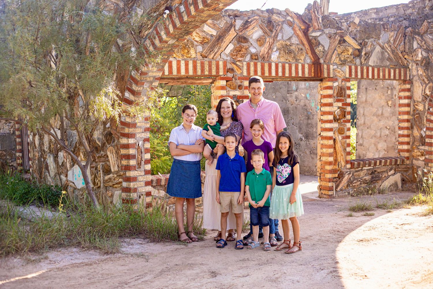 Family group photo standing under decorative brick archway outdoors.
