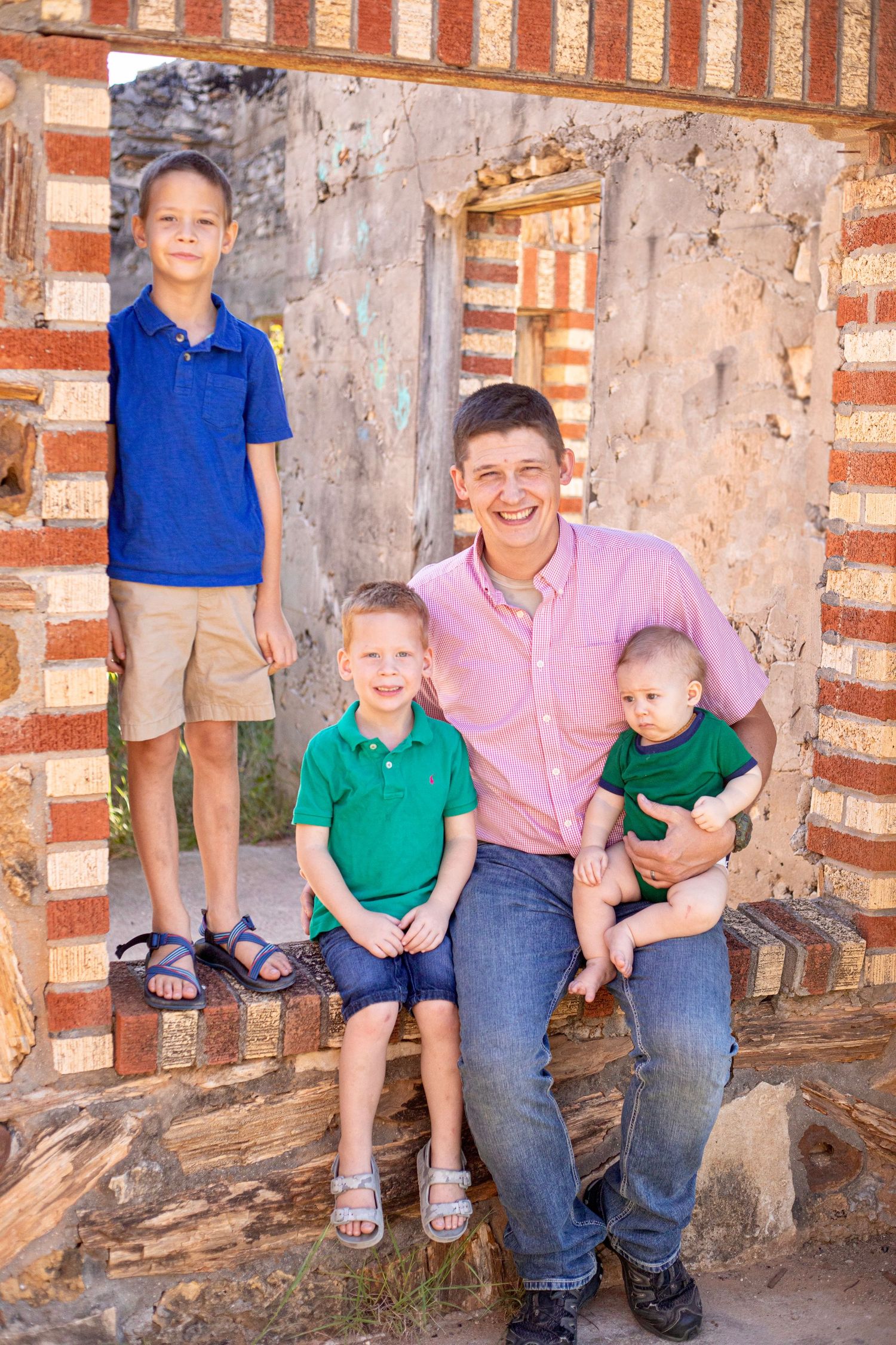 Family members seated on stone ledge against rustic brick and stone wall.