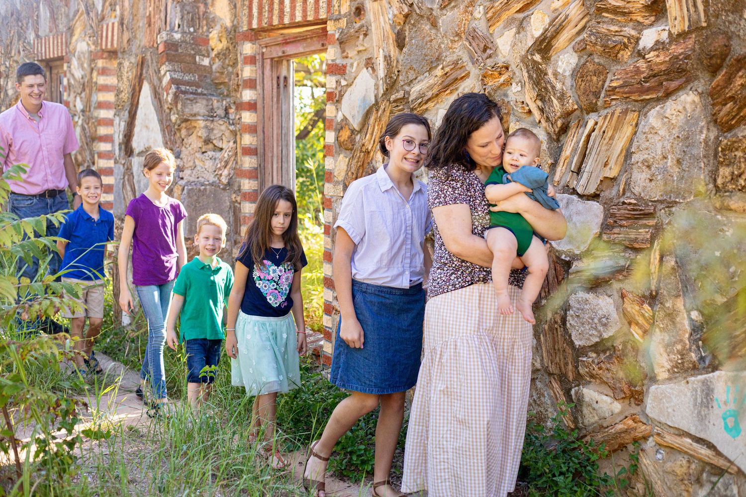 Group portrait against weathered stone wall with brick accents in garden setting.