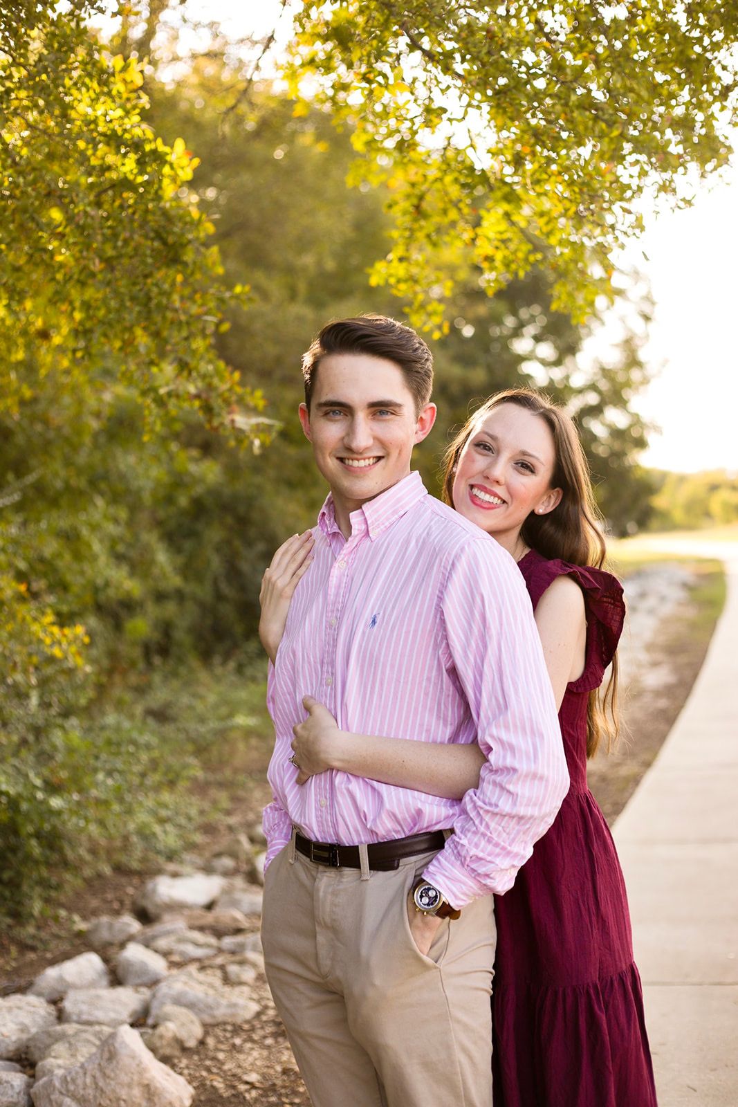 Couple in burgundy dress and pink shirt laughing together on outdoor path.