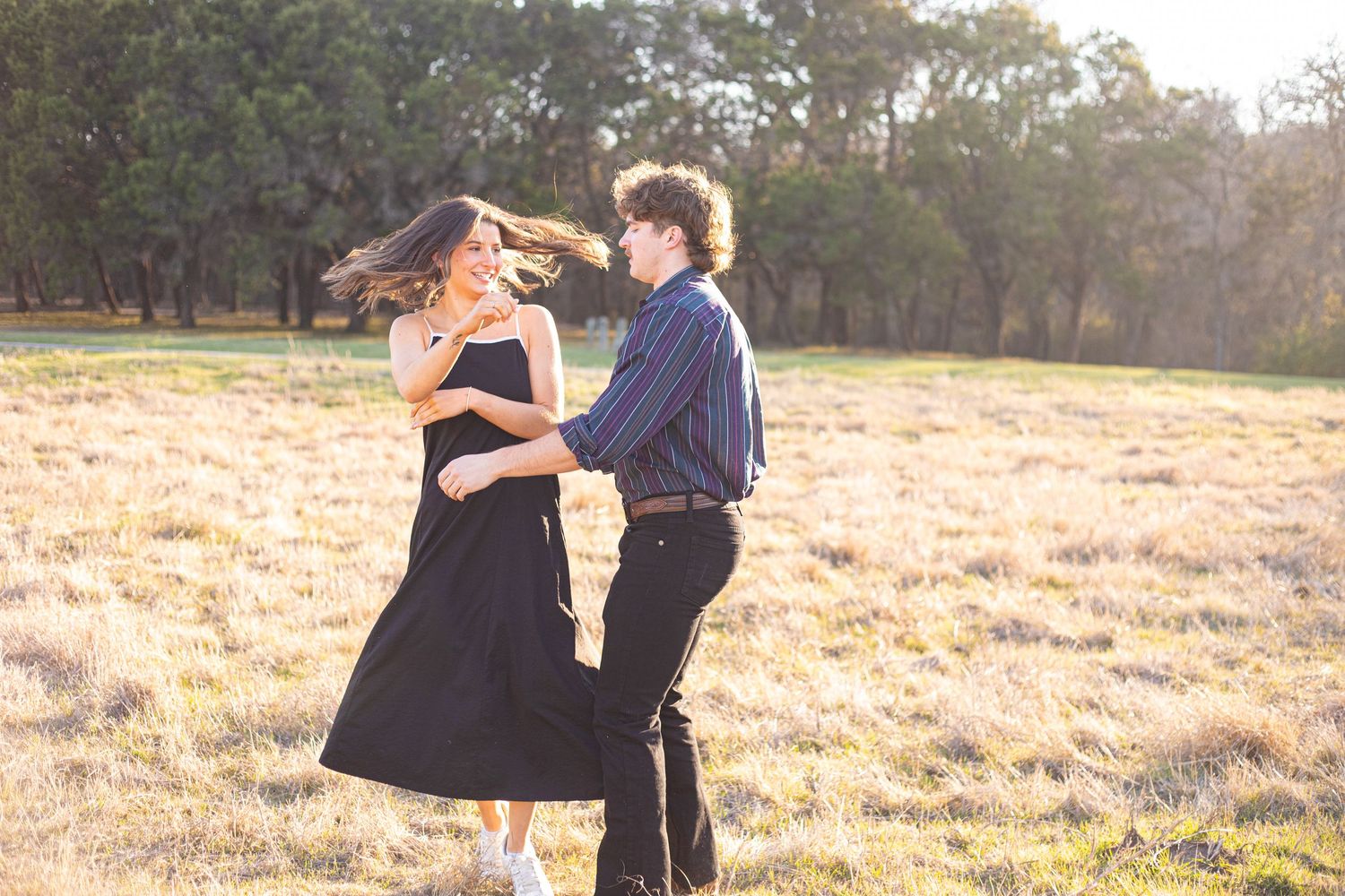 Couple embracing in a sunlit field with golden grass and trees in the background.